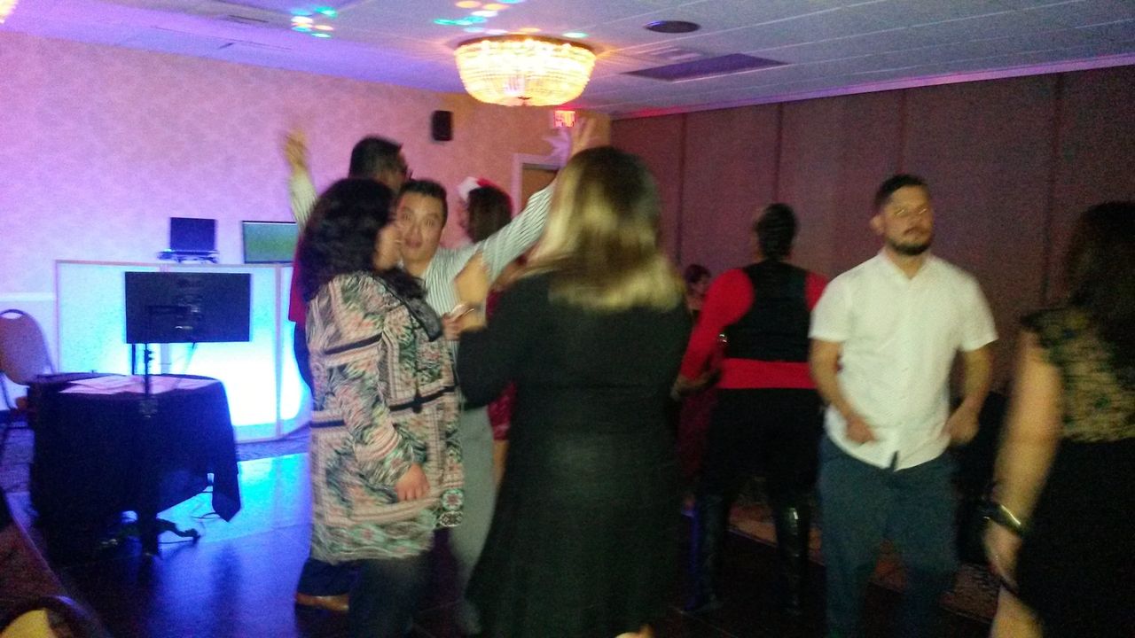 A group of people are dancing and socializing in a dimly lit room with a chandelier and a DJ setup in the background.