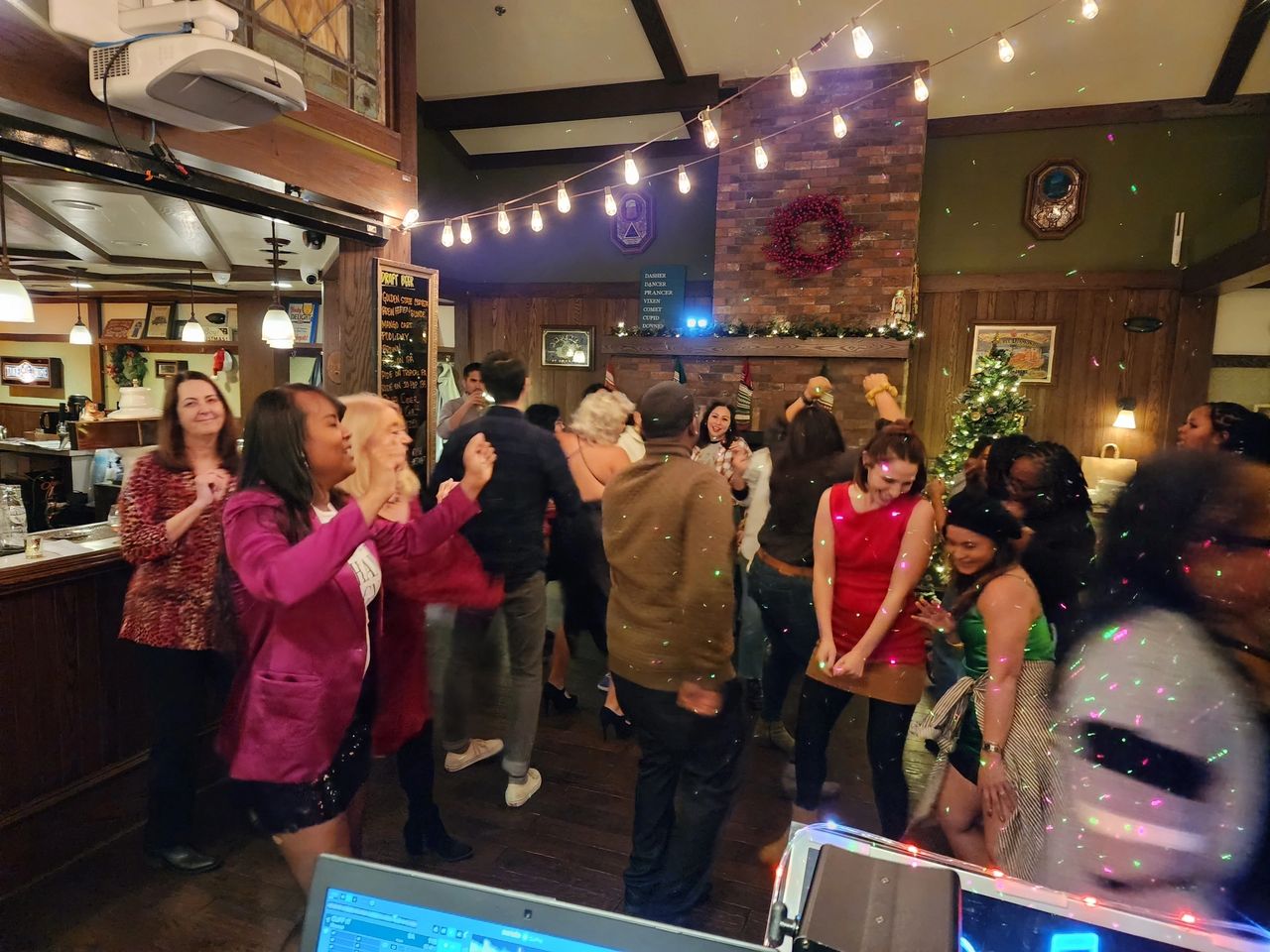 A group of people are dancing and socializing at an indoor party with festive lights and holiday decorations.
