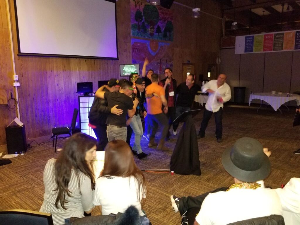 Party Dj 80s theme party. projector screen, some hugging and celebrating, while others sit and watch in a warmly lit room with wood-paneled walls.
