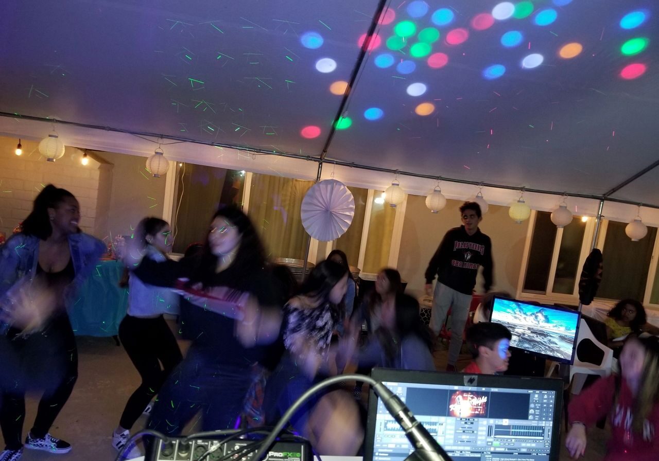 A group of kids dance under a tent with colorful lights as the kids karaoke dj plays a group dance song.