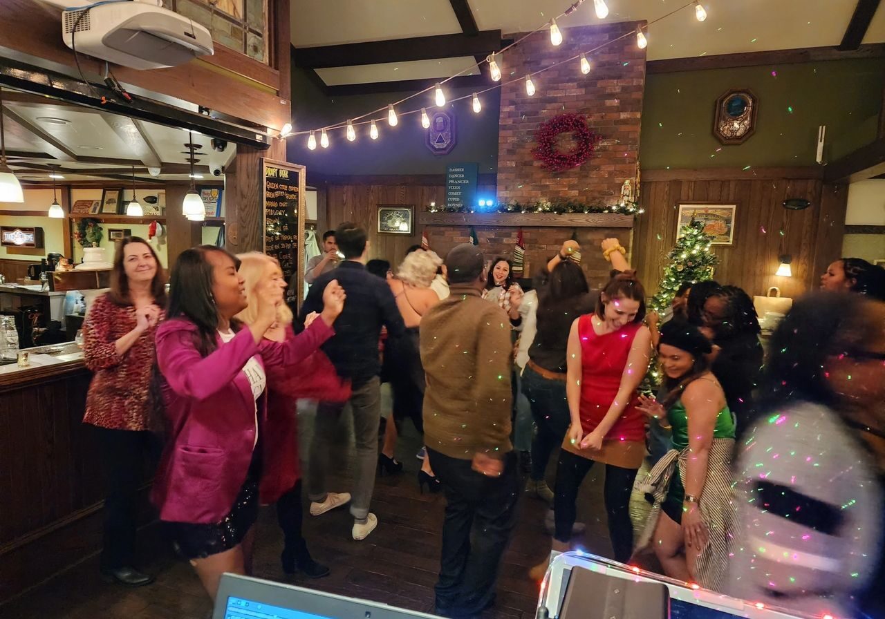 A group of people are dancing and socializing at an indoor party with festive lights and holiday decorations.