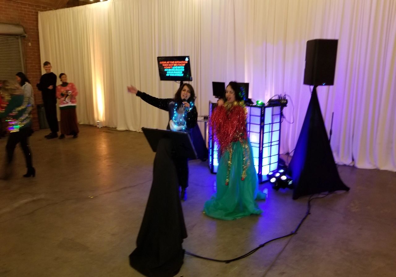 Two people singing with our karaoke dj party package with flat screen lyric displays, microphones and DJ equipment .